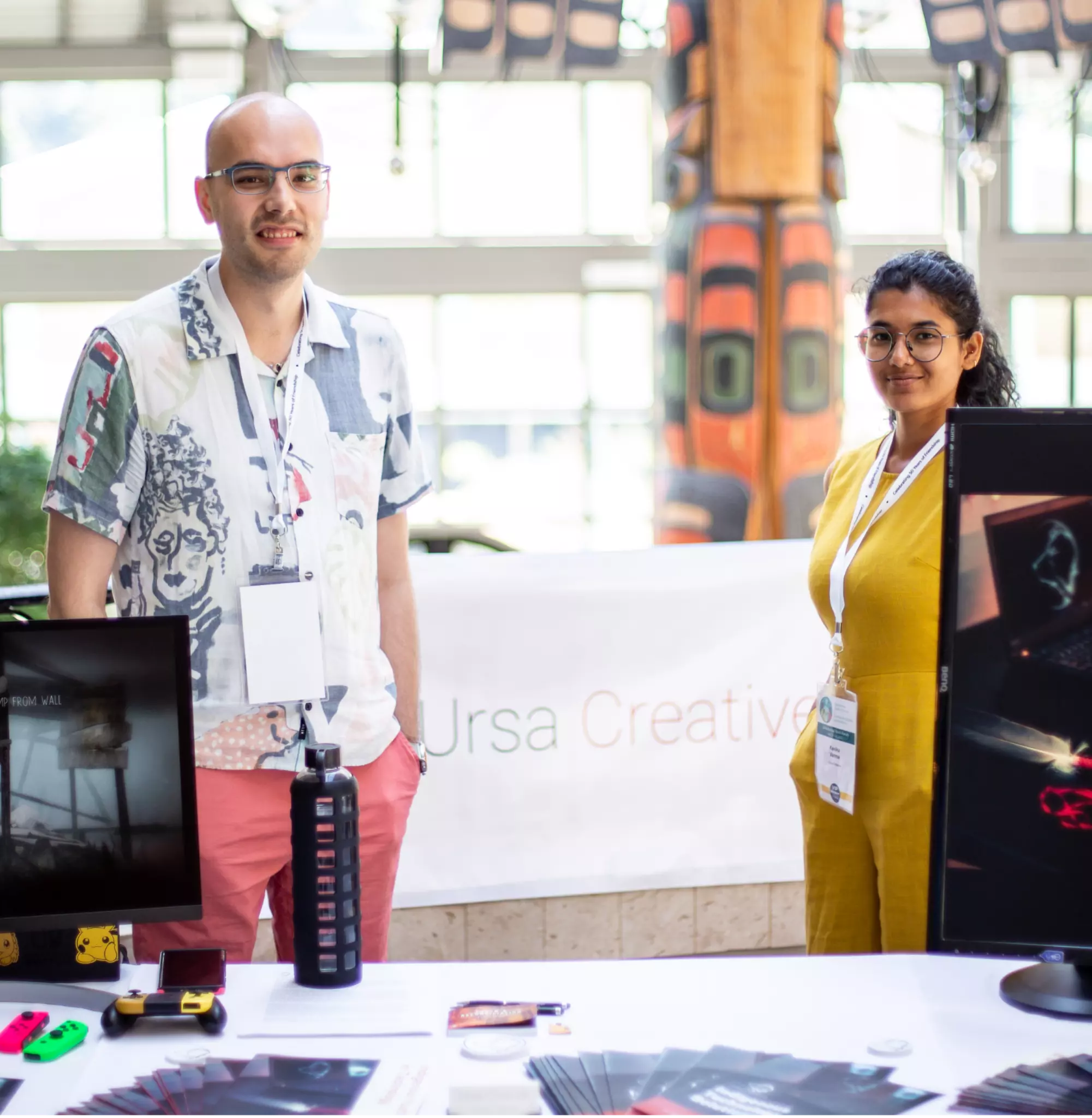 Two Ursa Creative members, Brendan Decontie and Kanika Verma, standing at a desk during a youth conference.