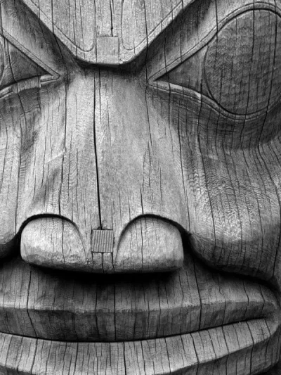 A black and white close up of a totem pole face.